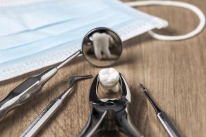 Tooth extraction concept with an array of stainless steel dental tools and a mask with the extracted tooth clasped in the pincers and reflected in the mirror